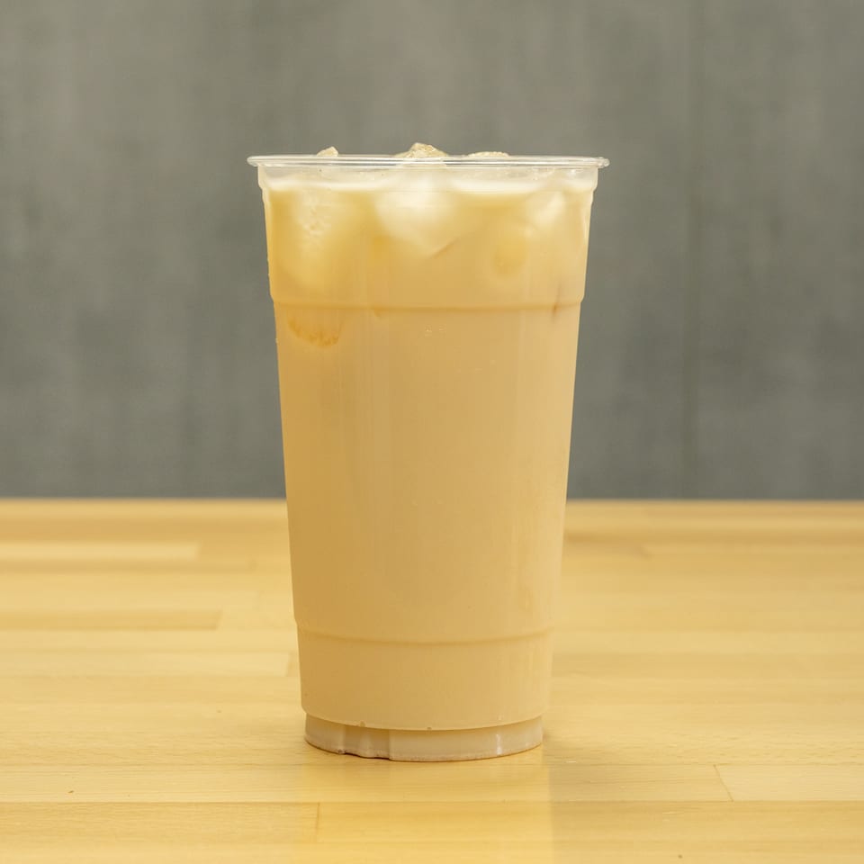 Clear plastic cup of pale yellow iced beverage on a wooden table against a gray background.