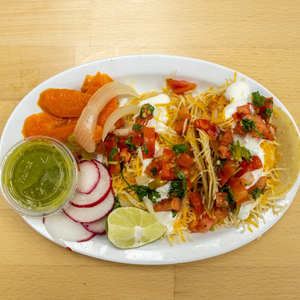 Loaded Mexican platter with tacos, shredded cheese, sour cream, pico de gallo, grilled vegetables, radishes, lime, and green salsa.