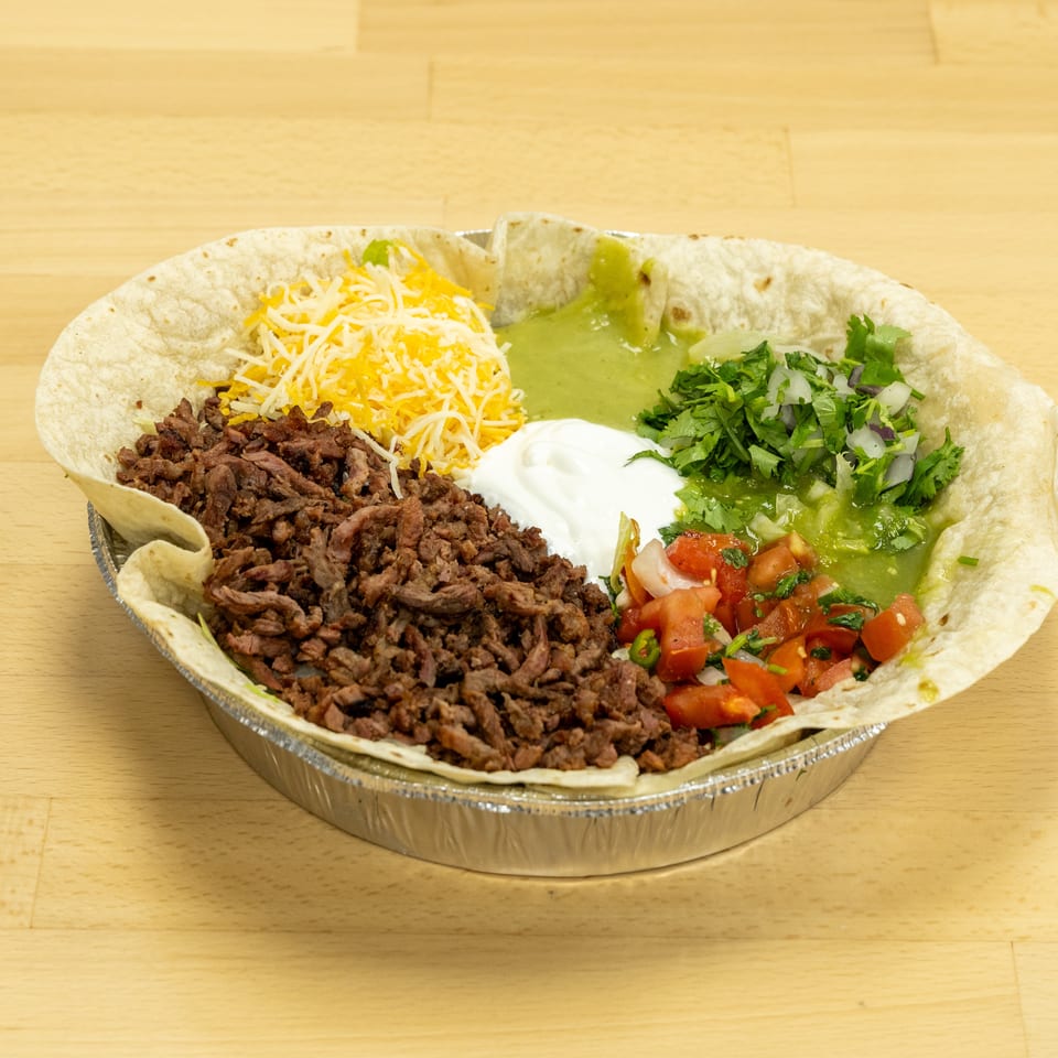 Mexican-style burrito bowl with carne asada, shredded cheese, guacamole, sour cream, cilantro, salsa, and tortillas.