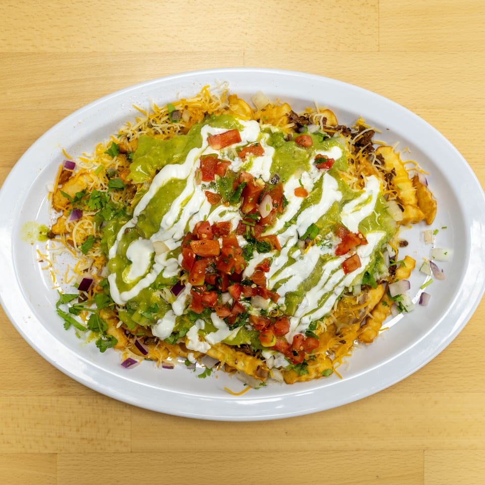 Loaded plate of nachos topped with melted cheese, guacamole, sour cream, pico de gallo, cilantro, onions, and seasoned meat.