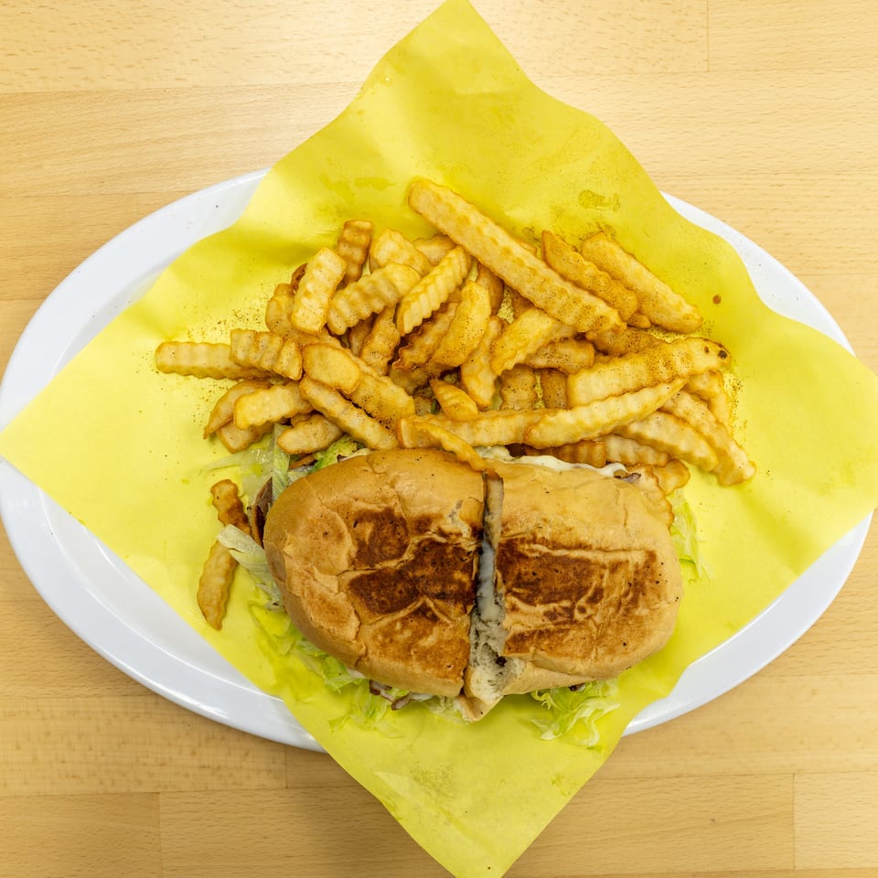Grilled sandwich with lettuce and sauce served alongside seasoned crinkle-cut fries on a paper-lined plate.