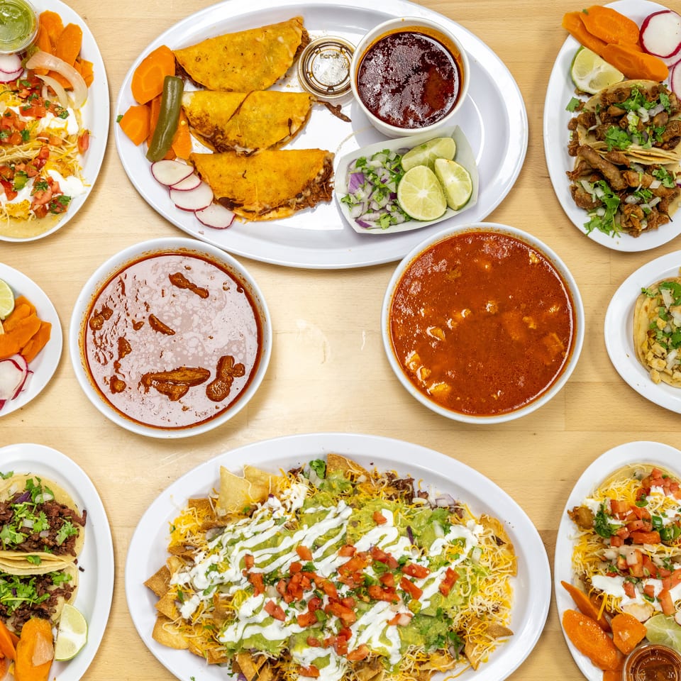 Overhead spread of Mexican dishes including tacos, quesadillas, nachos, enchiladas, soups, garnishes, and colorful salsas.